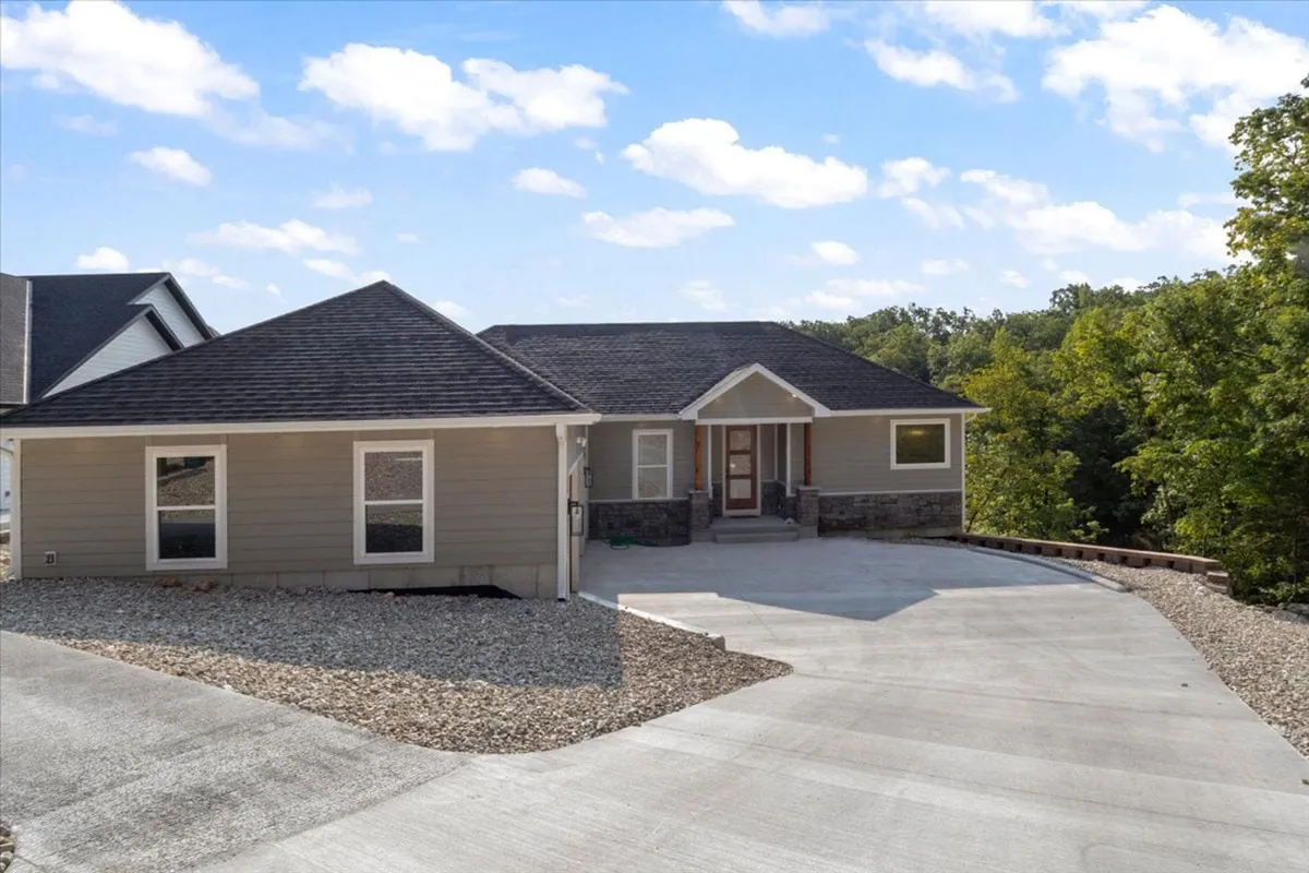 A welcoming view of the home's front entrance, framed by lush greenery and a spacious driveway. The porch invites gatherings, with ample space for relaxing outdoors and soaking in the natural setting. The surrounding landscape hints at easy access to nearby attractions and a tranquil retreat after a day of exploration.