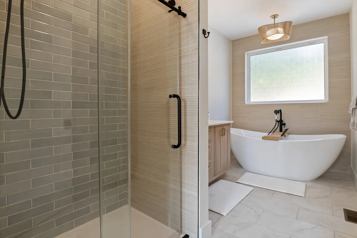 A luxurious, spa-inspired bathroom featuring a freestanding soaking tub next to a large window, a separate glass-enclosed shower, and abundant natural light. The clean lines and elegant fixtures create an atmosphere of indulgent relaxation, ideal for self-care and unwinding.