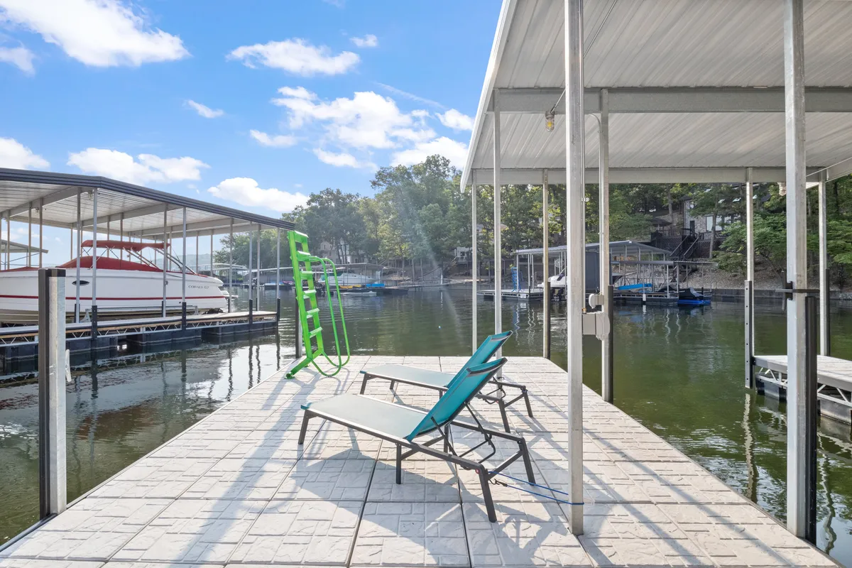 Lounge chairs arranged near boat docks and calm lake water, with a playful green slide leading into the water. The scene suggests fun swimming, sunbathing, and easy access to boating or paddleboarding, enhancing the sense of outdoor adventure.