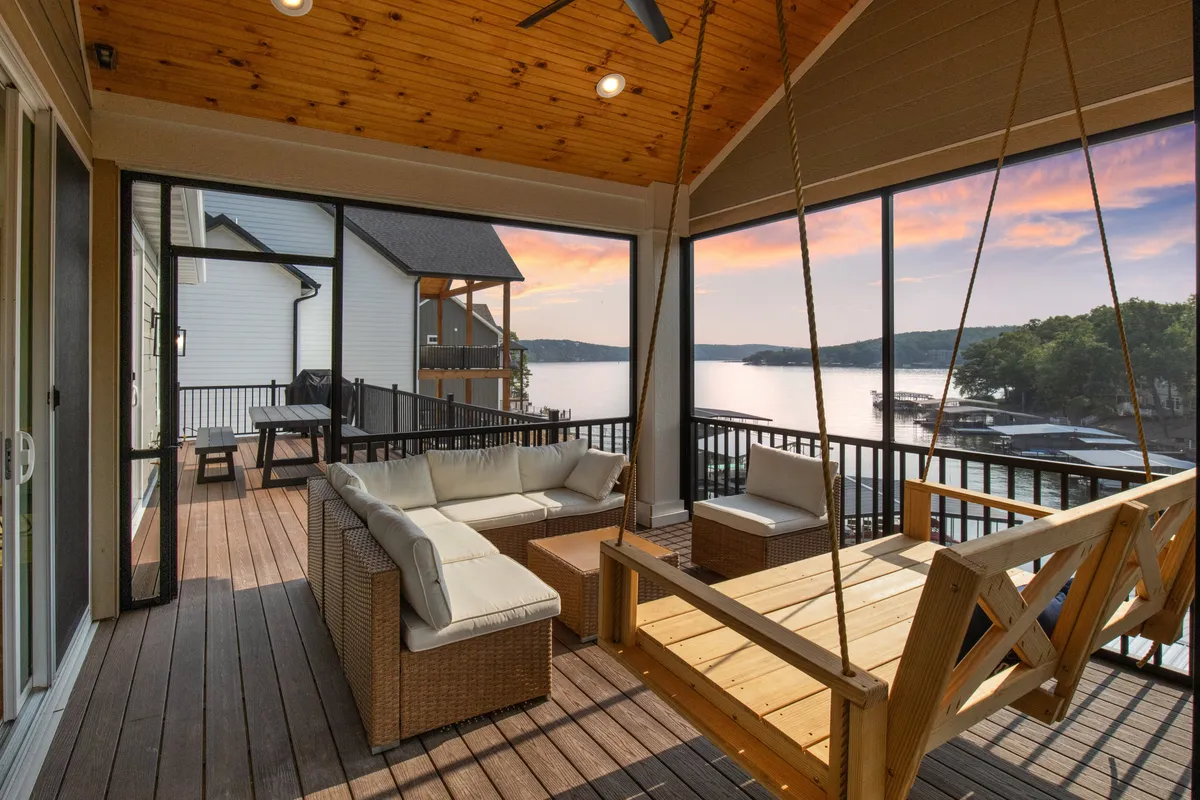 An inviting exterior seating area featuring a swing seat and comfortable chairs, all facing a beautiful lake view. The setting is perfect for unwinding after work or gathering for social conversation as the sun sets.