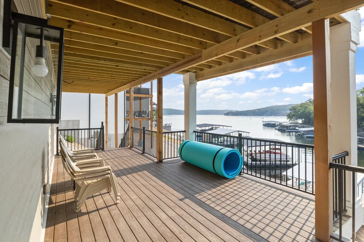 A lakeside deck with cozy seating and a clear view of the sparkling water, inviting guests to relax, entertain, or enjoy water activities. A blue water tube hints at playful opportunities by the shoreline.
