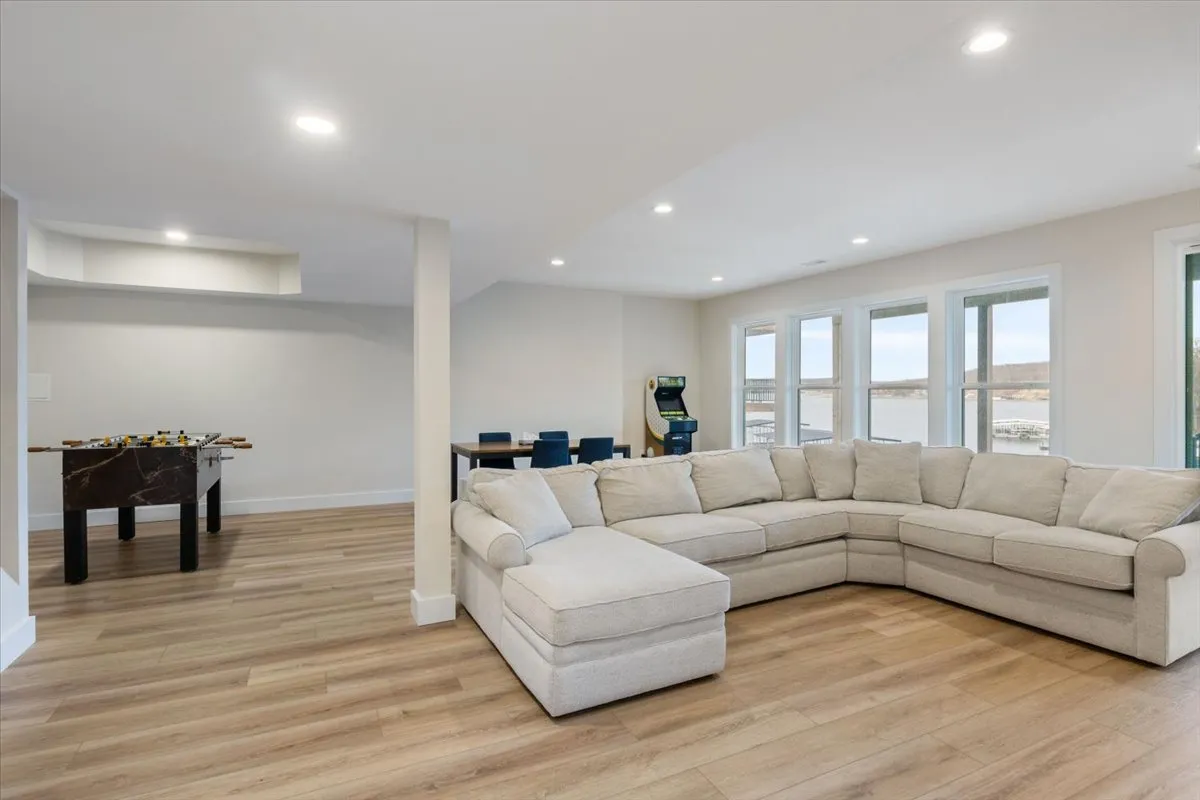 A spacious entertainment room with a large sectional sofa, game table, arcade machine, and expansive windows overlooking scenic views. The space is perfect for socializing, playing games, and relaxing, with the natural light enhancing the welcoming atmosphere.