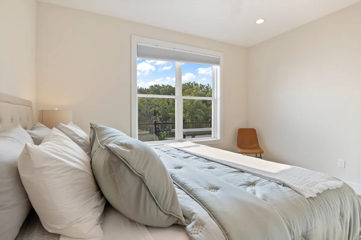 A tranquil bedroom with a plush bed and large window offering a beautiful view of nature and the lake. The natural light floods the room, and a modern chair provides a comfortable seating area for reading or reflection.