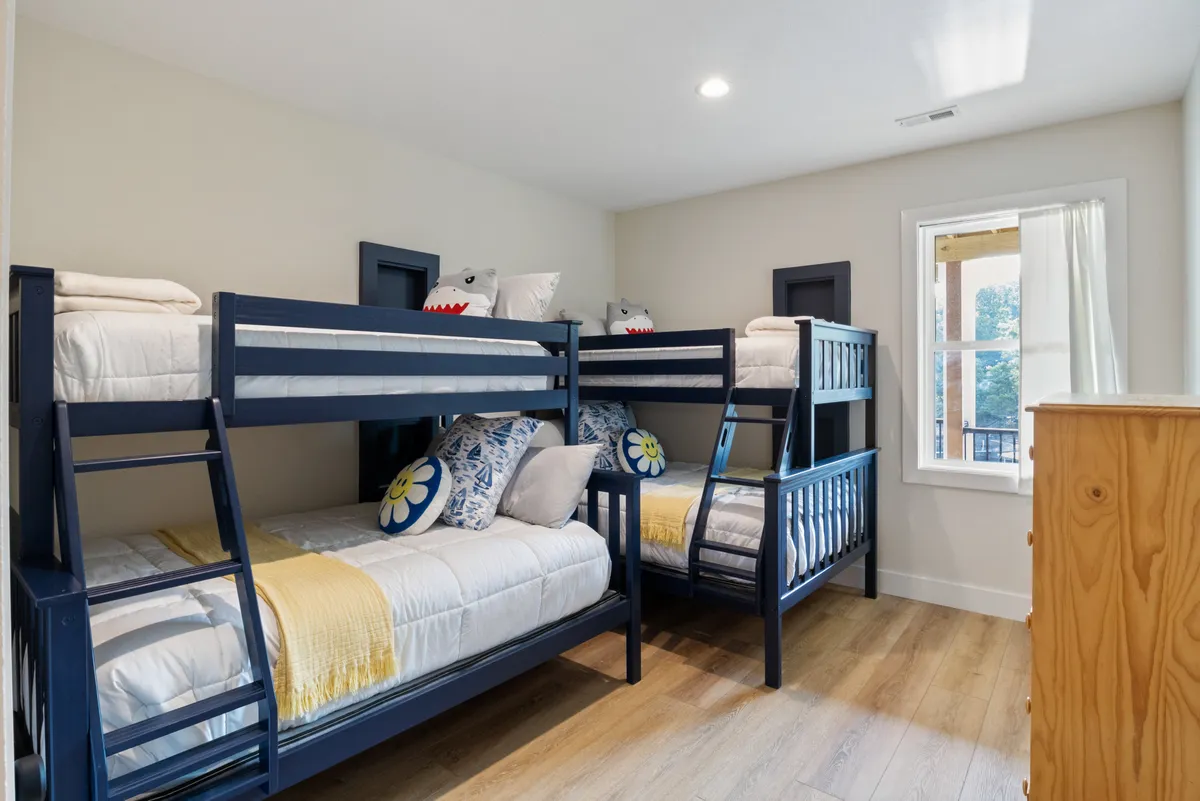 A playful and comfortable bunk room featuring dual twin-over-full bunk beds adorned with decorative pillows and a wooden dresser. The space is bright, inviting, and clearly designed to delight both children and adults, with cozy bedding and room for shared experiences.